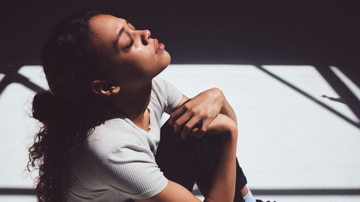 Mental health, sad woman sitting and isolated in room with tears on her face. Anxiety or depression, psychology or trauma patient and insomnia or depressed scared young female person sit alone